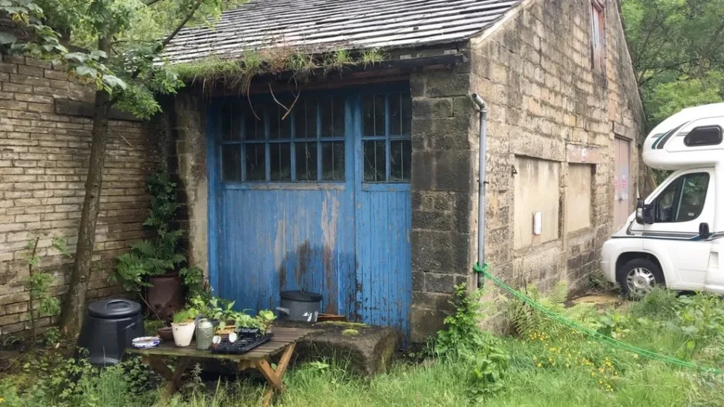 The stable before renovation, with its old blue doors and overgrown yard