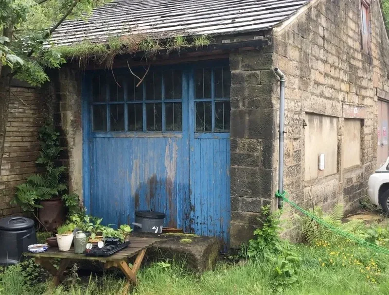 The stable before renovation, with its old blue doors and overgrown yard